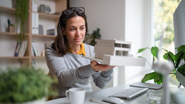 Das Bild zeige eine Frau, die ein Modell eines Hauses in der Hand hält. 