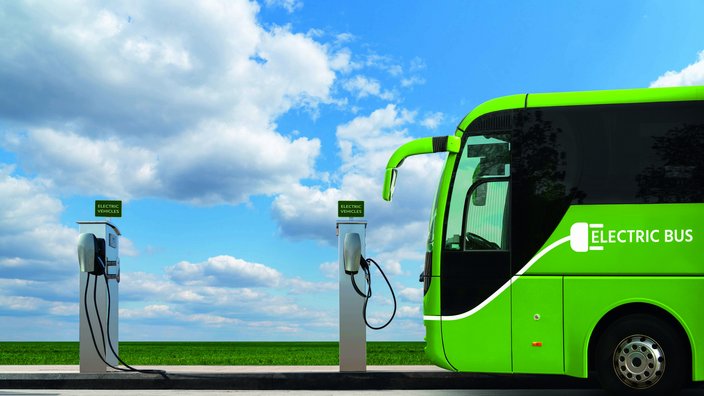 Das Bild zeigt einen grünen E-Bus bei einer Ladestation stehend.