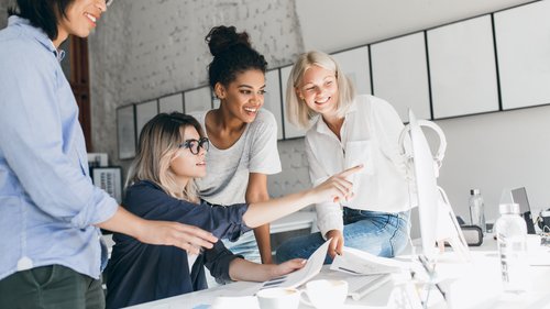Das Bild zeigt vier Frauen sitzend und stehend um einen Schreibtisch. Alle vier Frauen schauen auf den Bildschirm.