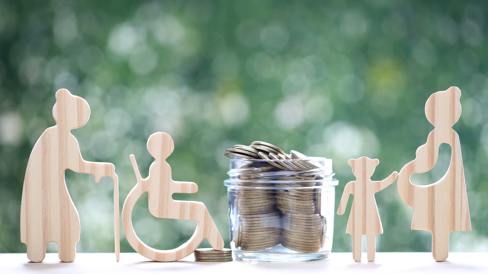 Verschiedene Holzfiguren, die unterschiedliche Lebenslagen darstellen und ein Glas mit Münzen