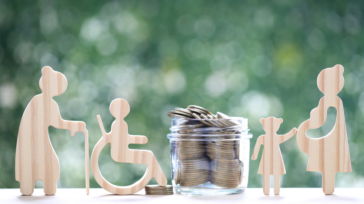 Verschiedene Holzfiguren, die unterschiedliche Lebenslagen darstellen und ein Glas mit Münzen