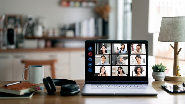 Das Bild zeigt einen Laptop auf einem Tisch. Auf dem Bildschirm des Laptops sind Bilder von Personen zu sehen, wie bei einer Online-Konferenz.