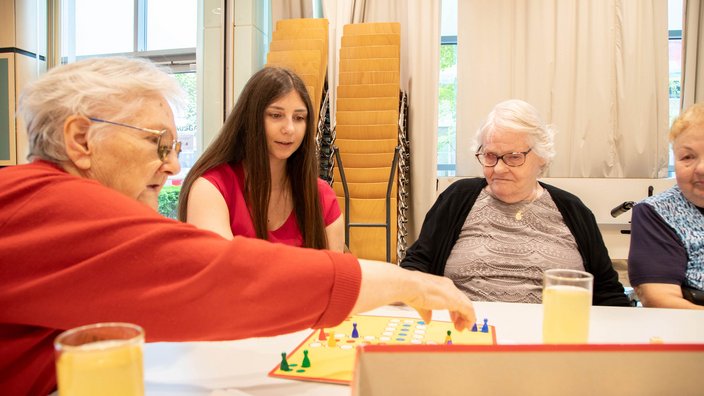 Eine Gruppe alter Damen spielt mit einer jungen Frau Mensch ärgere dich nicht