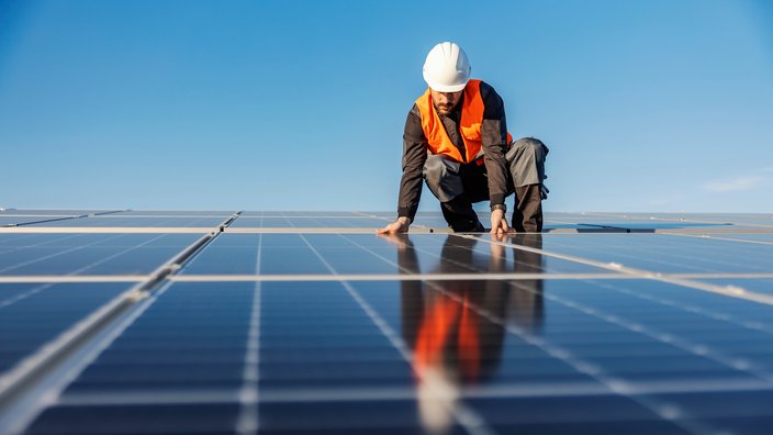 Das Bild zeigt einen Mann, der auf einem Photovoltaikdach arbeitet.