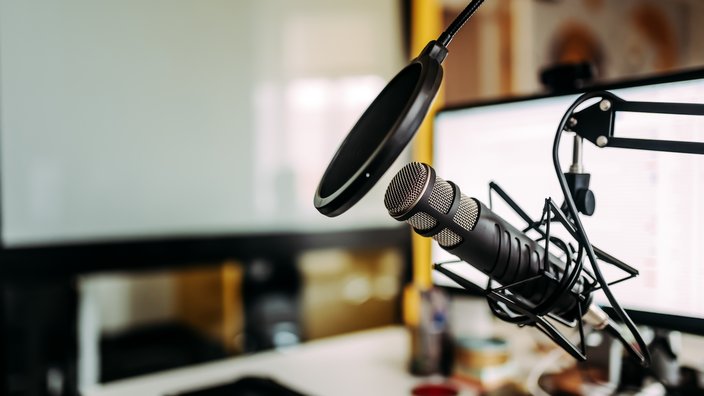 Das Bild zeigt ein Podcast Microphon vor einem Arbeitsbildschirm.