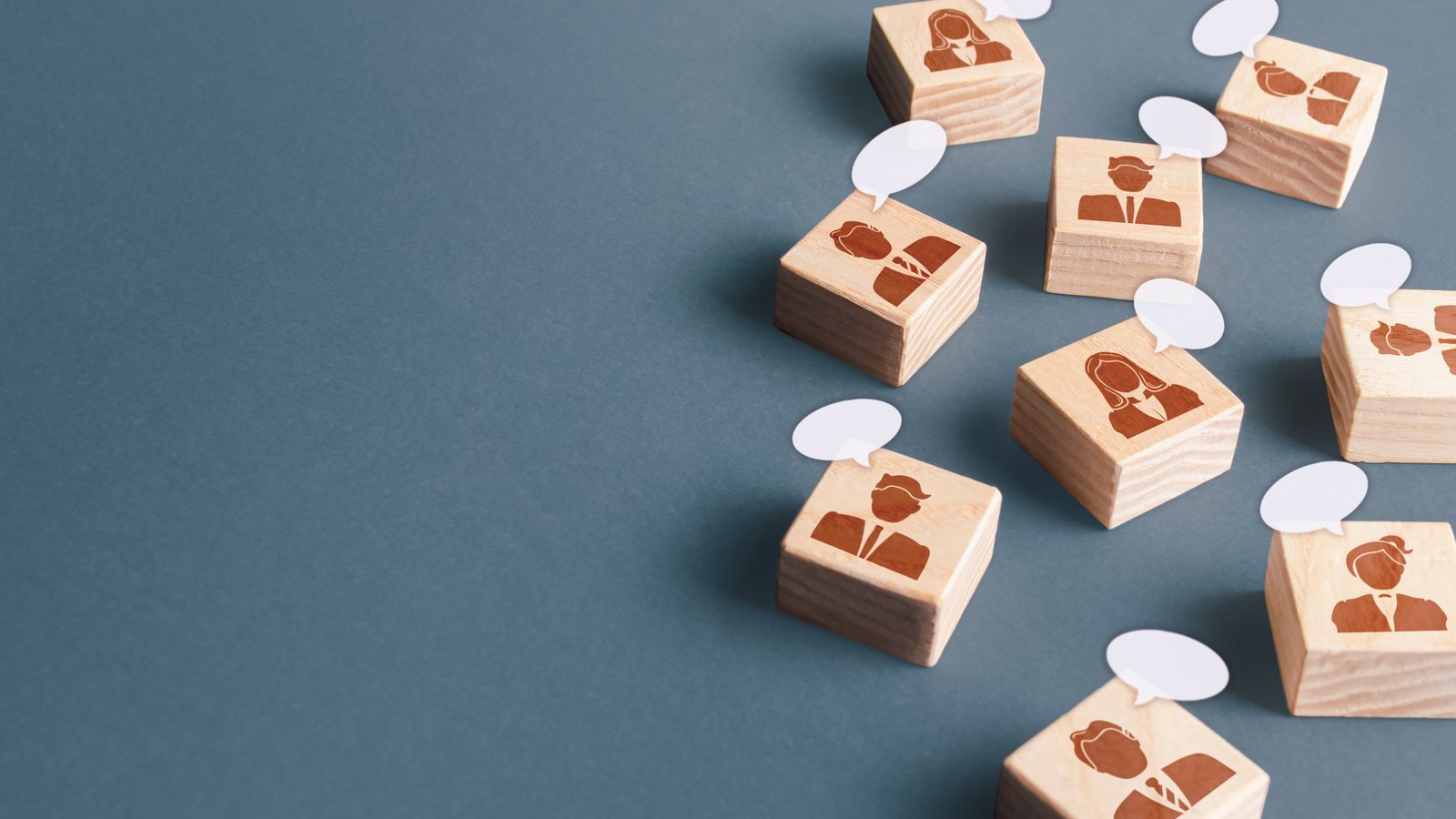 Holzbausteine mit stilisierten Menschen in Businesskleidung, jeweils mit einer kleinen weißen Sprechblase.