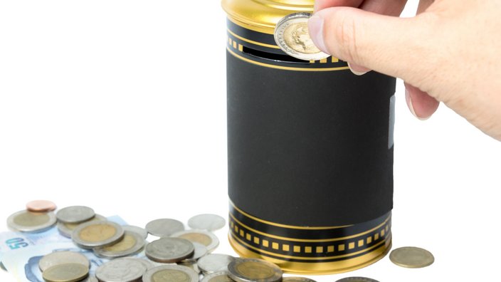Foto einer Hand, die Münzen in eine Spardose einwirft