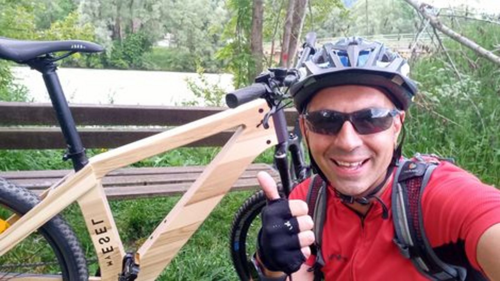 Das Foto zeigt einen Mann mit Sonnenbrille und Radhelm, der mit einem E-Bike aus Holz im Wald unterwegs ist. 