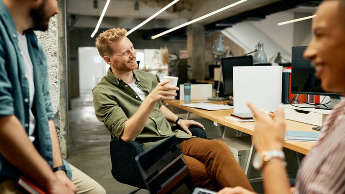 Teamwork in moderner Arbeitsumgebung Das Bild zeigt drei Männer lachend in einer Gesprächssituation an ihrem Arbeitsplatz..