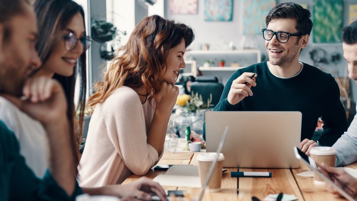 Das Bild zeigt fünf Personen an einem Besprechungstisch sitzend mit einem Laptop.
